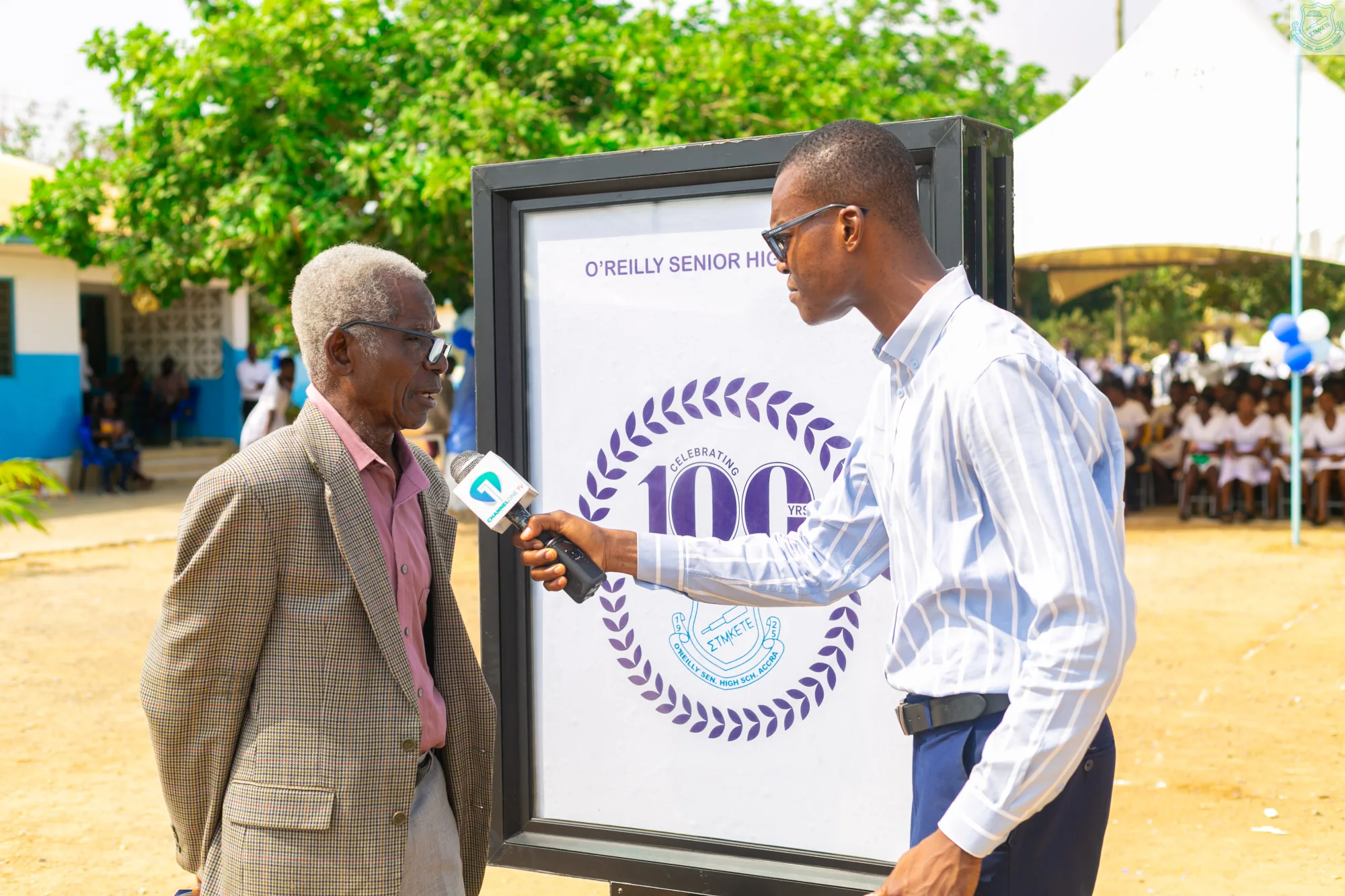 An older alumnus speaking beside the centenary display