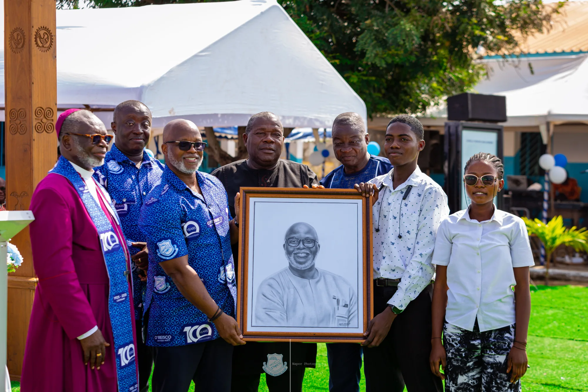 Older alumni gathered around a framed portrait at a school ceremony